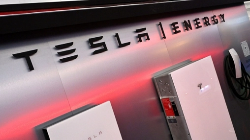 Tesla Energy signage with white home battery storage units mounted on display wall with ambient red lighting