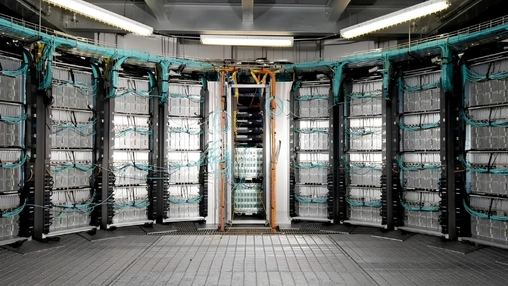A curved wall of server racks densely packed with teal fibre optic cables in a large data centre facility