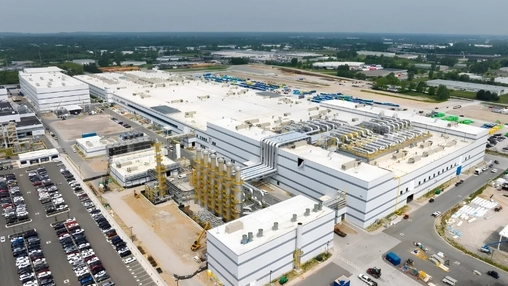 Drone shot of an industrial facility with white buildings, yellow cranes, and rooftop mechanical systems.
